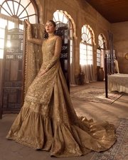 Naisha by Mastorat – A Timeless Expression of Luxury Introducing Naisha by Mastorat, a breathtaking couture ensemble that celebrates Pakistan's rich heritage of hand embroidery and luxury craftsmanship. Designed for brides and women who appreciate timeless elegance, Naisha is an extraordinary combination of traditional artistry and contemporary sophistication. Every motif, embellishment, and fabric selection has been thoughtfully curated to create a statement outfit that radiates grace and grandeur. Crafted from premium quality khaadi net, this luxurious ensemble features intricate hand embellishments across the shirt, sleeves, and farshi gharara, paired with an elegant plain net dupatta finished with heavily ornamented borders. The rich detailing and meticulous craftsmanship make Naisha a masterpiece suitable for weddings, bridal events, receptions, engagements, festive celebrations, and formal occasions. The ensemble showcases a harmonious balance between traditional aesthetics and refined luxury. The delicate khaadi net base serves as the perfect canvas for intricate handwork, allowing every embellishment to shine beautifully while maintaining a soft and graceful silhouette. Exquisite Handcrafted Embellishments The beauty of Naisha lies in its remarkable handcrafted detailing. Skilled artisans spend countless hours carefully embellishing each panel using traditional embroidery techniques passed down through generations. The shirt features a mesmerizing tessellated jaal pattern adorned with: Hand-cut sequins Dabka work Naqshi embroidery Fine resham embroidery Traditional zardozi craftsmanship Delicate cut dana detailing Elegant tilla embroidery Together, these luxurious embellishments create an artistic composition that sparkles beautifully from every angle while maintaining a refined and graceful appearance. The intricate jaal extends throughout the shirt, complemented by elegant linear embellishment patterns that enhance the elongated silhouette, making the outfit exceptionally flattering. Elegant Floral Artistry Adding warmth and sophistication to the design are blooming floral motifs embroidered in contrasting shades of rich red resham. These vibrant florals beautifully complement the golden embellishments, creating a striking visual balance between tradition and modern luxury. The floral embroidery is thoughtfully integrated into the overall design, offering texture, depth, and timeless elegance without overwhelming the delicate khaadi net fabric. Premium Hand Embellished Shirt Naisha includes a fully hand embellished shirt crafted from luxurious khaadi net. The shirt features: Hand embellished front Hand embellished back Intricately decorated sleeves Fine luxury finishing Elegant neckline detailing Traditional craftsmanship Premium quality fabric Its lightweight construction allows for graceful movement while offering exceptional comfort throughout long wedding ceremonies and celebrations. Regal Farshi Gharara The luxurious farshi gharara serves as the highlight of this couture ensemble. Carefully embellished by hand, the gharara features rich ornamental detailing that enhances its majestic volume and flow. Every movement reflects the brilliance of handcrafted embroidery, making it an unforgettable statement piece. Its traditional silhouette captures the timeless charm of Mughal-inspired fashion while remaining elegant and sophisticated for today's modern woman. Whether worn for a wedding, nikkah, mehndi, baraat, reception, or formal event, the farshi gharara elevates the entire look with unmatched grandeur. Sophisticated Net Dupatta Completing the ensemble is a premium plain net dupatta adorned with exquisitely embellished borders. The gold-toned dupatta perfectly complements the intricate embroidery of the shirt and gharara while adding an ethereal finishing touch. Its delicate drape enhances the luxurious aesthetic without overpowering the outfit. A contrasting red chaddar further enriches the overall styling, creating a stunning combination of classic bridal colors and traditional elegance. Premium Fabric Details Naisha is crafted using carefully selected luxury fabrics to ensure both elegance and comfort. Included Pieces Hand Embellished Khaadi Net Shirt Front Hand Embellished Khaadi Net Shirt Back Hand Embellished Khaadi Net Sleeves Hand Embellished Khaadi Net Farshi Gharara Hand Embellished Plain Net Dupatta Each component is designed to complement the others, resulting in a perfectly coordinated couture ensemble. Perfect for Special Occasions Naisha is ideal for: Bridal Wear Wedding Functions Baraat Nikkah Ceremony Reception Engagement Events Mehndi Celebrations Formal Gatherings Festive Occasions Luxury Eid Collection Family Celebrations Its timeless design ensures it remains a treasured addition to any luxury wardrobe for years to come. Exceptional Craftsmanship Every Naisha outfit reflects the dedication and expertise of experienced artisans. The intricate handwork requires extensive hours of meticulous craftsmanship, making each ensemble uniquely special. The harmonious blend of traditional embroidery techniques with premium fabrics creates a couture piece worthy of life's most memorable celebrations. Styling Suggestions Complete your bridal or formal look by pairing Naisha with: Traditional kundan jewelry Polki bridal sets Statement jhumkas Gold heels Embellished khussa Elegant clutch bag Soft glam makeup Classic bridal hairstyle The versatile design allows for both heavily accessorized bridal looks and elegant minimalist styling. Care Instructions To preserve the beauty of your handcrafted ensemble: Dry clean only. Store in a garment bag. Avoid direct sunlight for extended periods. Handle embellishments with care. Do not machine wash. Steam lightly when needed. Proper care will help maintain the richness of the embroidery and fabric for years. Important Note Please note that the actual product color may vary slightly from the images displayed due to lighting conditions during photography and differences in screen resolutions. As each outfit is individually handcrafted, slight variations in embellishments are considered part of its unique artisanal charm. Shipping Information Estimated Shipping Time: 3–4 Months Since Naisha is a handcrafted luxury couture outfit, every order is prepared with exceptional attention to detail to ensure the highest standards of quality and finishing before dispatch. Experience timeless elegance with Naisha by Mastorat, where traditional craftsmanship meets contemporary luxury to create a masterpiece worthy of your most cherished occasions.